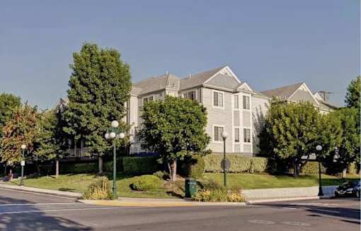 A large house with a grey roof and white walls is surrounded by trees and bushes.