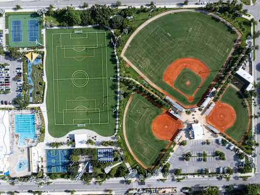 An aerial view of a sports complex with a soccer field, baseball diamonds, and a swimming pool.