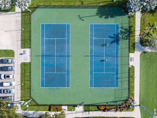 Two tennis courts surrounded by a green fence.