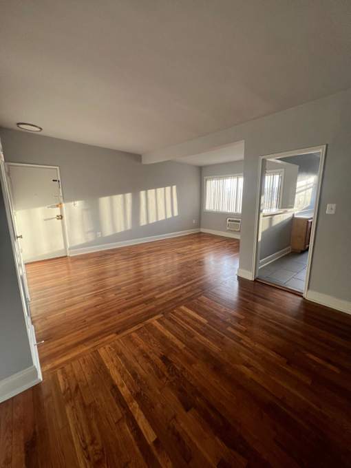 A room with wooden flooring and a door on the left side.