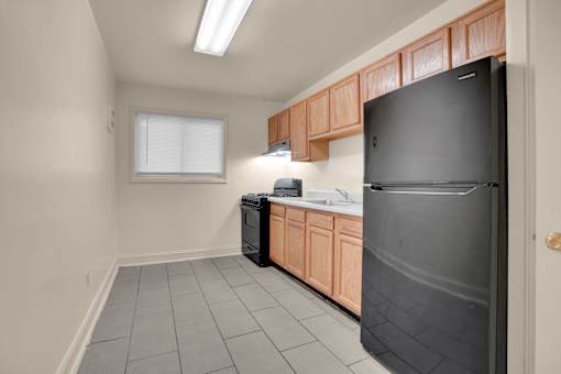 A kitchen with a black refrigerator, wooden cabinets, and a window.