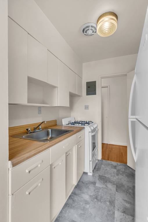 A kitchen with a white refrigerator, wooden countertop, and white cabinets.
