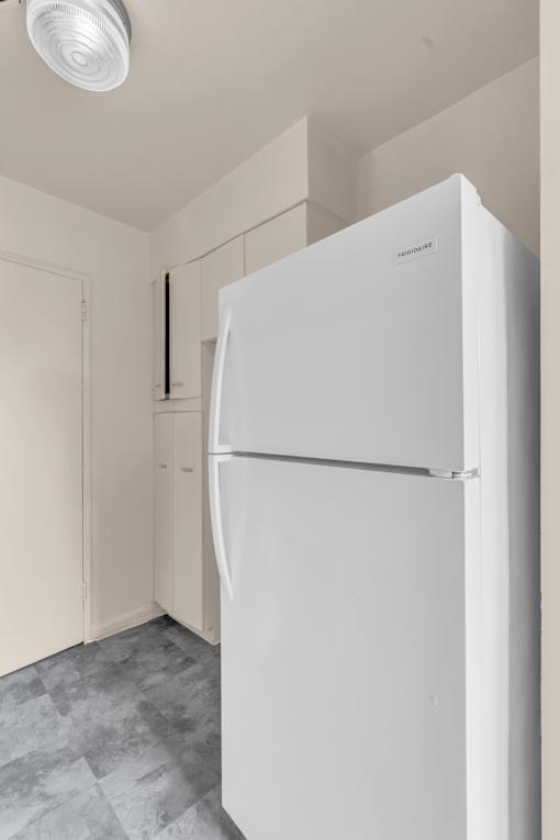 A white refrigerator in a kitchen with a grey floor.
