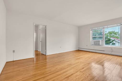 A room with a wooden floor and a window showing a view of trees and a house.