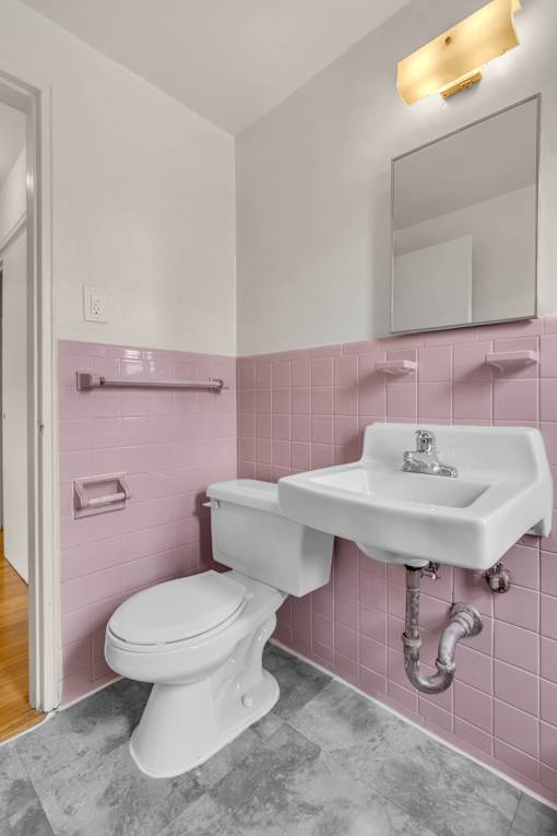 A white toilet in a pink tiled bathroom.