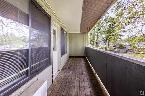 A balcony with a wooden floor and a view of trees and houses.