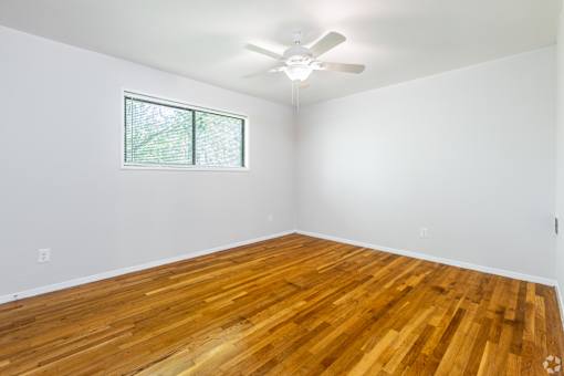 A room with a ceiling fan and a window with a view of trees.