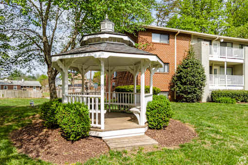 A gazebo is in the middle of a grassy area in front of a brick building.