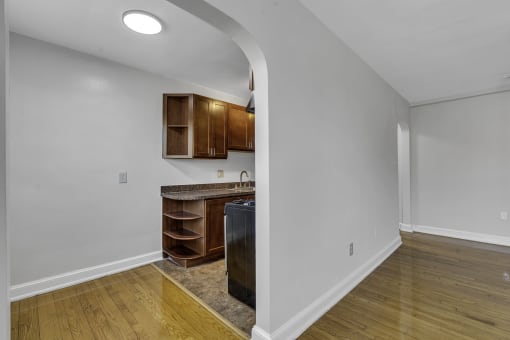 a living room with a kitchen with wooden floors and white walls