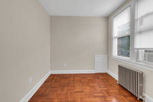 a living room with wood flooring and a radiator and two windows