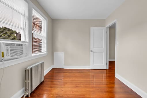 an empty living room with wood floors and a radiator and a window