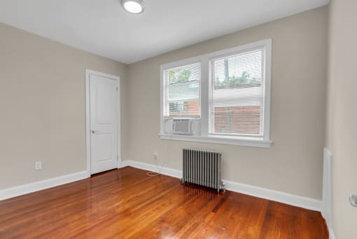 an empty living room with wood floors and a radiator and a window
