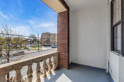 A balcony with a brick pillar and concrete floor overlooks a street.