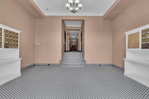 A hallway with a chandelier, stairs, and a wall of mailboxes.
