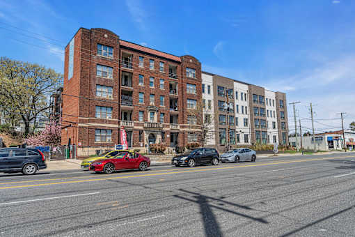 A red car is parked on the side of the road in front of a brick building.