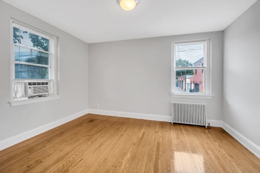 an empty room with wood flooring and two windows