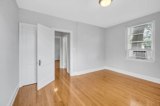 a bedroom with white walls and wood floors and a window