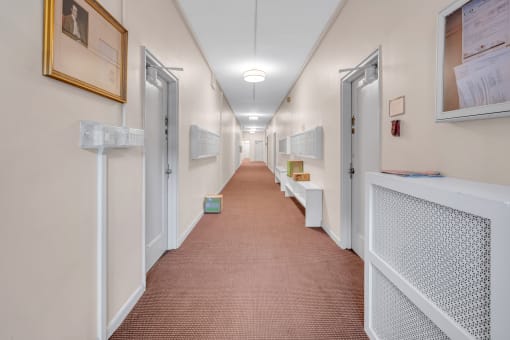 a long corridor with doors and paintings on the walls and a red carpeted floor