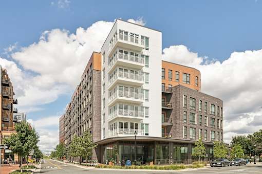 A modern multi-story building with a white and brown facade is situated on a street corner with cars parked in front.