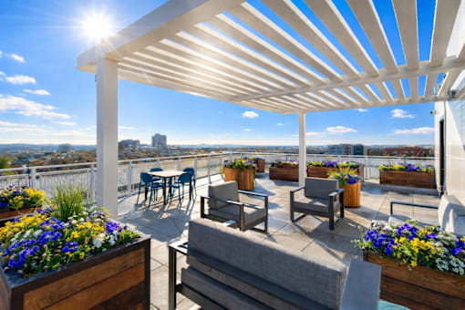 A patio with a white pergola and wooden furniture overlooking a cityscape.