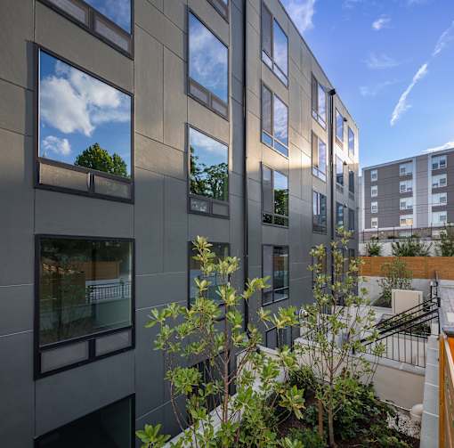 A modern building with grey walls and windows reflecting the sky and trees.