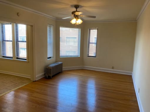 an empty living room with a ceiling fan and three windows