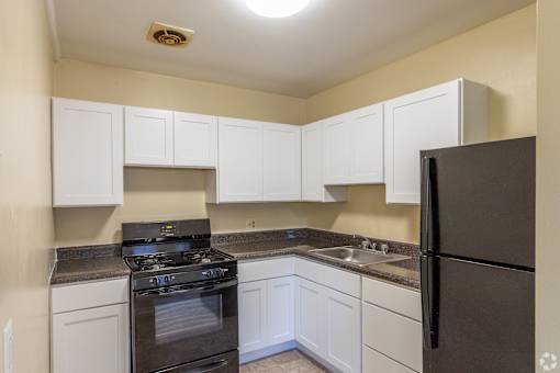 A kitchen with white cabinets and a black refrigerator.