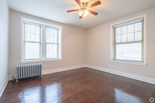 A room with a ceiling fan and two windows.