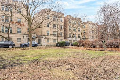 A grassy area in front of apartment buildings with cars parked in the background.
