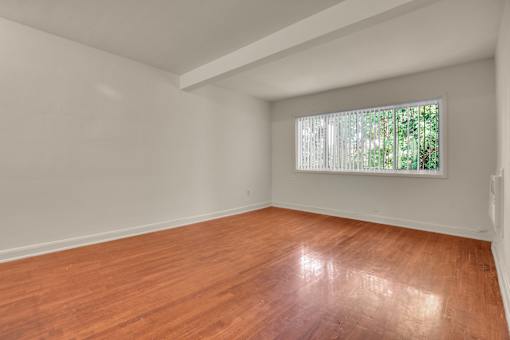 Empty room with wooden floor and a window with blinds.