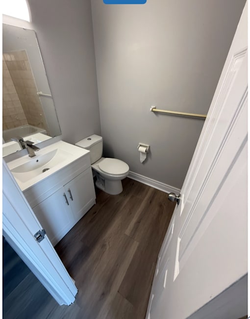 A white bathroom with a toilet, sink, and a wooden floor.