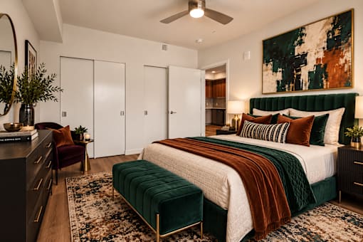 A bedroom with a large bed and a green velvet ottoman.