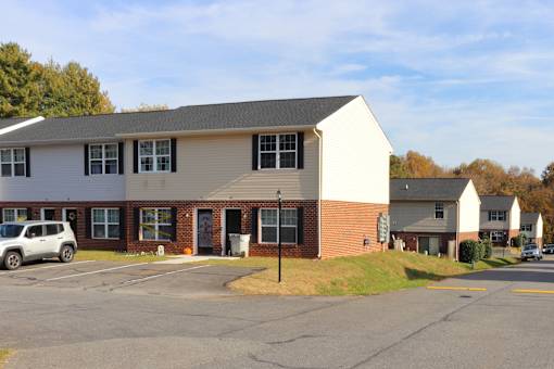 A white building with a grey roof and a parking lot in front.