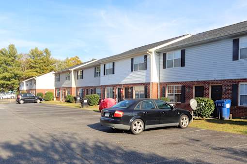 A black car is parked in a parking lot in front of a white and red building.