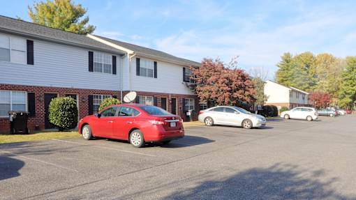 A red car is parked in a parking lot in front of a building.
