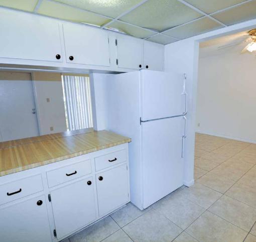 A white kitchen with a refrigerator, cabinets, and a counter.
