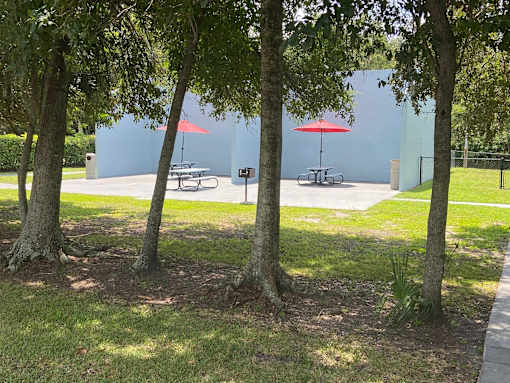 A park with trees, picnic tables, and umbrellas.