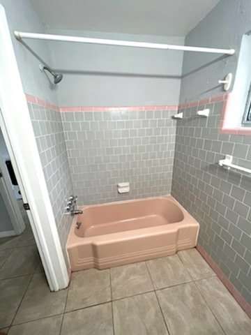 A small pink bathtub in a bathroom with grey tiles.