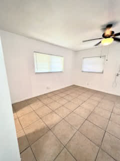 A room with a ceiling fan and two windows.