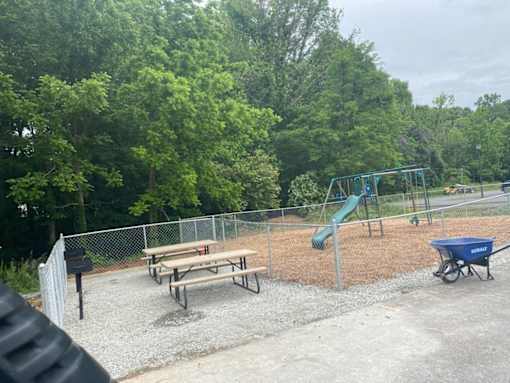 A playground with a slide, picnic table, and a blue wheelbarrow.