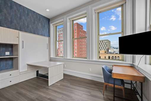 A room with a desk and chair in front of a window with a view of a city.