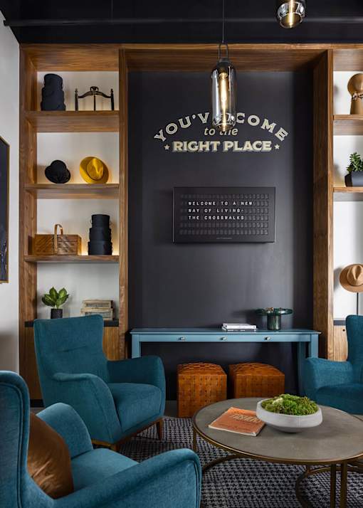 A living room with a grey wall and a wooden shelf with a sign that says "You're welcome to my right place".