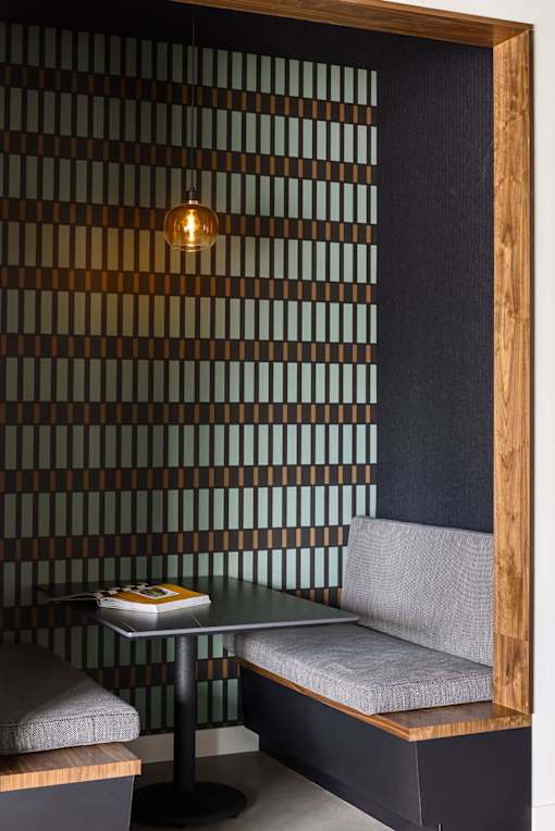 A small table with a book on it and a grey cushioned bench in front of a wall with a wooden frame.