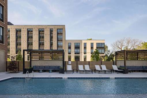 A pool in front of a building with a bench and chairs.