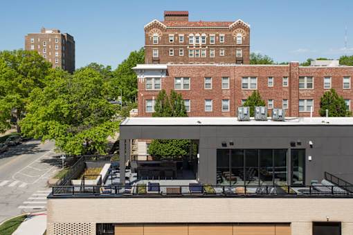 A modern building with a balcony is in front of a red brick building.