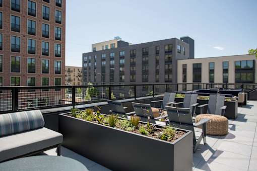 A rooftop patio with a planter box and chairs.