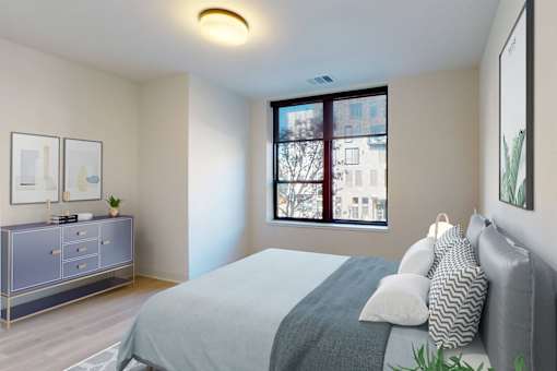 A bedroom with a bed, nightstand, and a window with a view of a city.