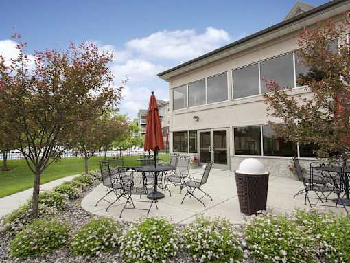 A patio with a table and chairs is surrounded by trees and flowers.