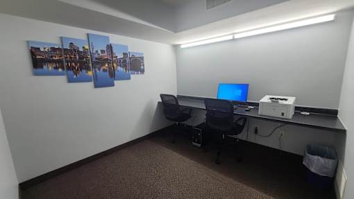 A room with a desk, computer, and pictures on the wall.