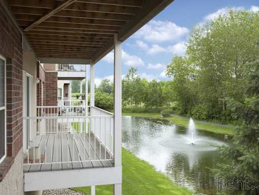 A house with a balcony overlooking a pond with a fountain.